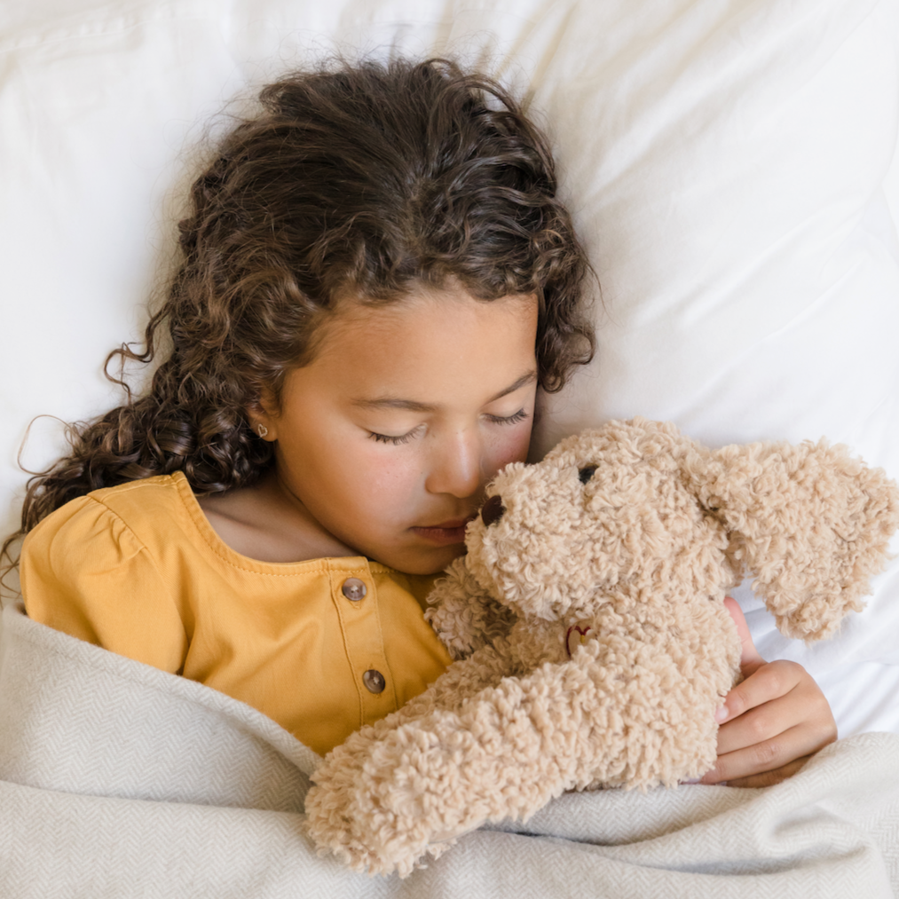 Little girl laying in bed wearing a gold jumper and snuggling with mediTATE